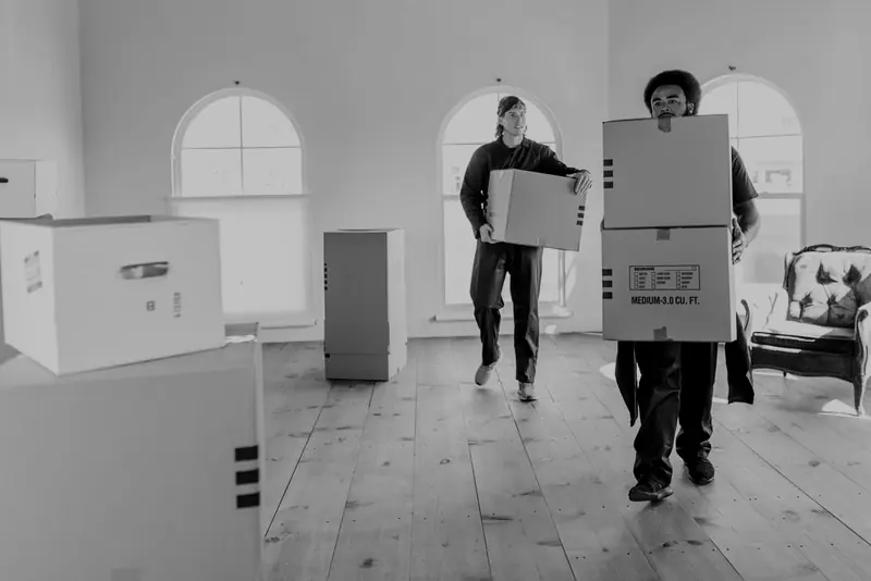 Two people moving boxed household belongings through a room