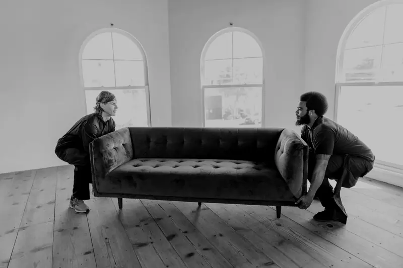 Two people carrying a sofa across a room during a furniture removal job